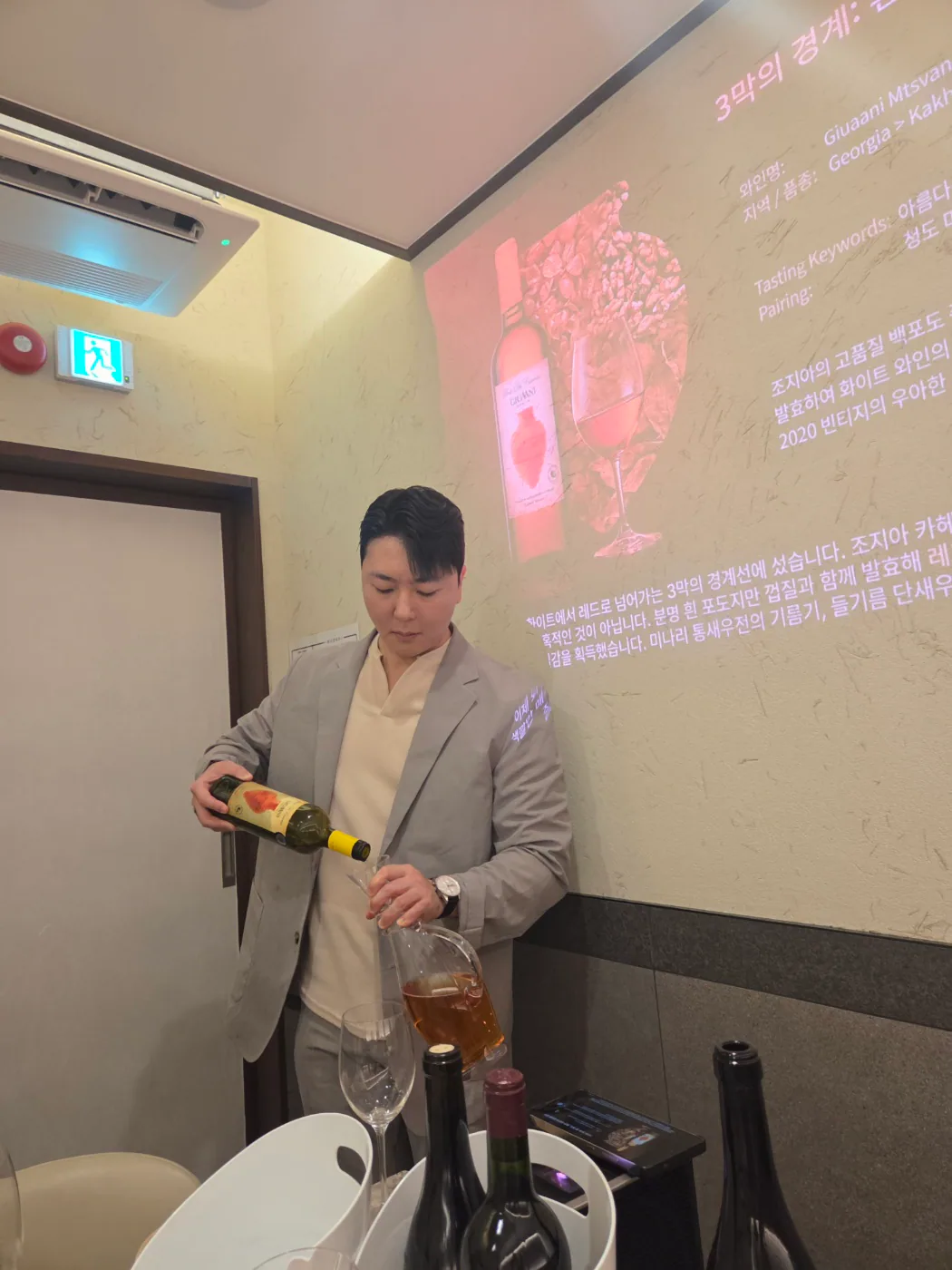 프레젠테이션 화면 앞에서 Giuaani Mtsvane Qvevri 2020을 디캔터에 따르는 장면