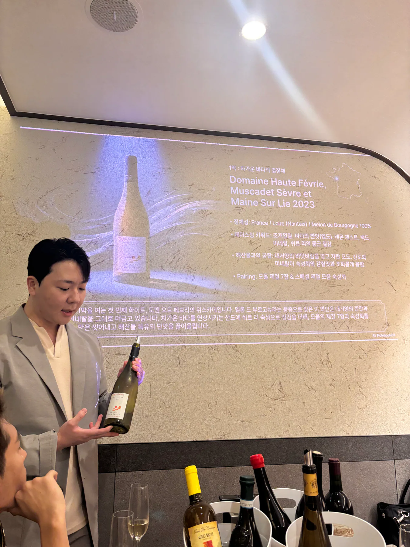 Domaine Haute Févrie Muscadet Sèvre et Maine Sur Lie 2023 슬라이드 앞에서 병을 설명하는 장면