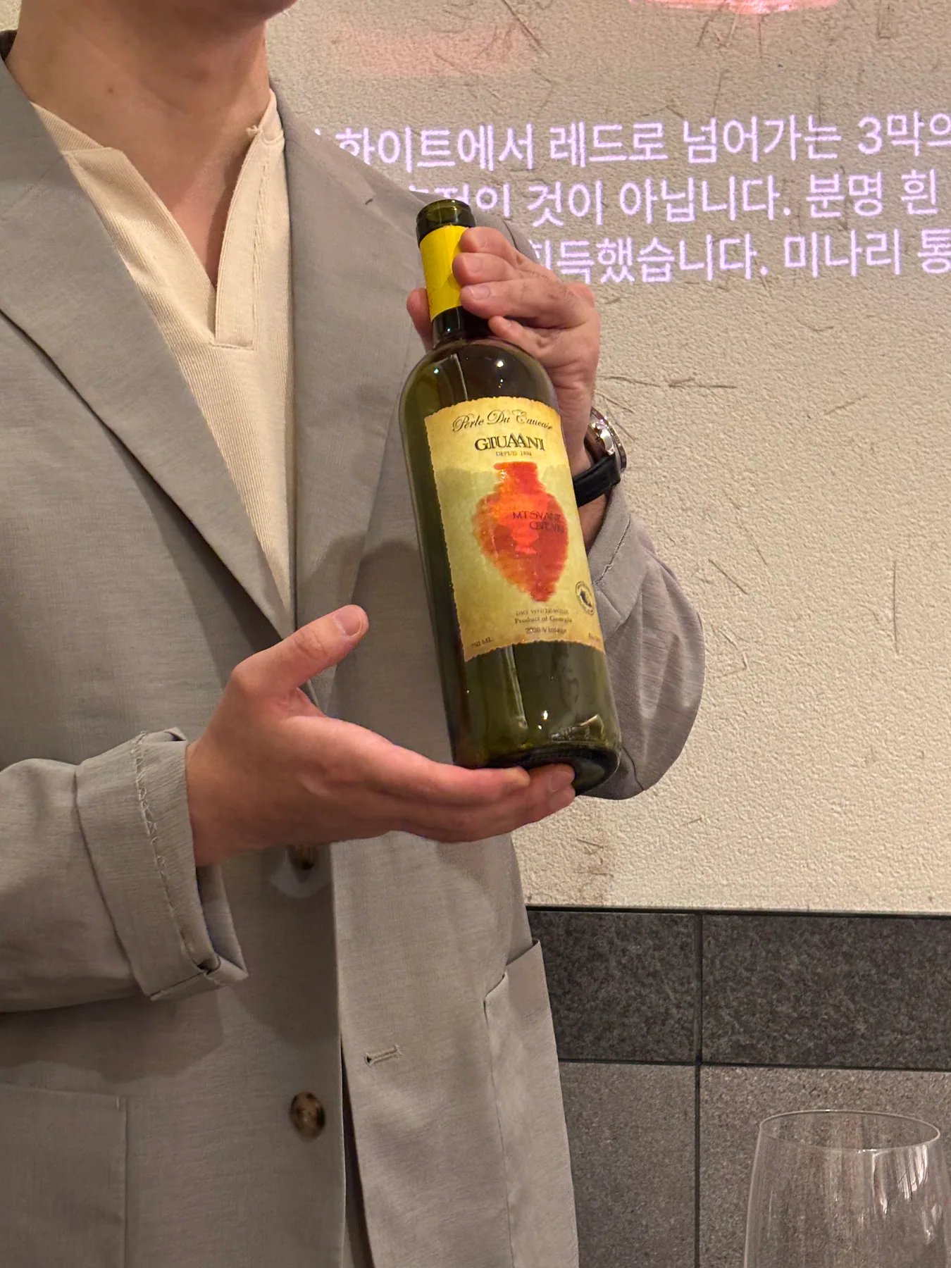 3막의 전환을 설명하며 Giuaani Mtsvane Qvevri 2020 병을 보여주는 장면